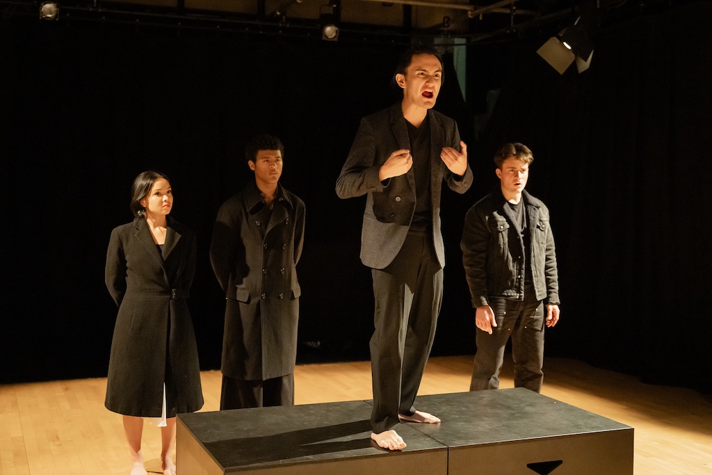 Actor stands on a black riser with three other actors standing behind him during the final presentation of The Winter's Tale